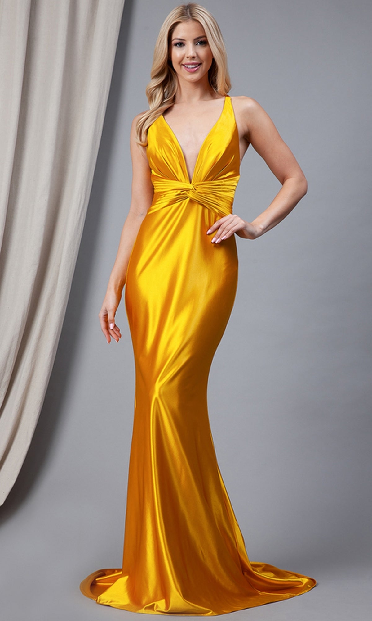 A woman stands against a neutral gray background wearing the Twist-Waist Deep V-Neck Long Prom Dress 5039—a sleeveless, floor-length gold satin gown with a deep V-neckline.